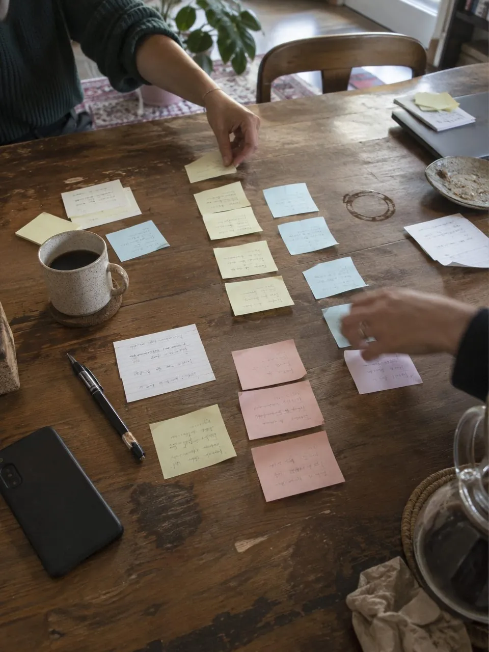 Two people arranging handwritten cards on a table to set priorities